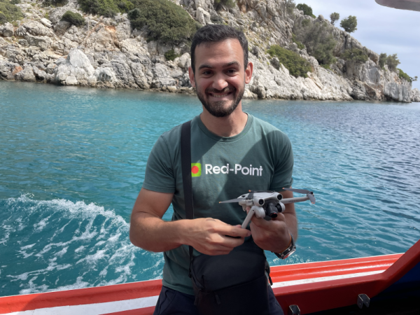 A man wearing a Red-point t-shirt holding a drone outside.